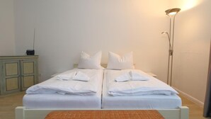 A double bed with white linens, a small table with a woven placemat, and a floor lamp. - Appartement Kiek in 09 Westerland (Westerland)