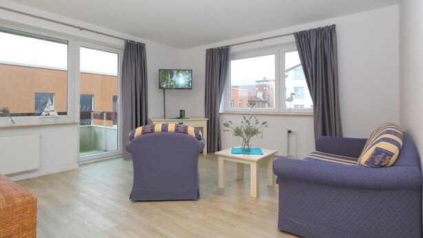A modern living room with two sofas, a TV, and a view of a building through large windows. - Appartement Kiek in 09 Westerland (Westerland)