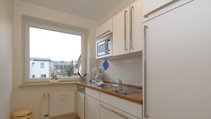 A small kitchen with a window, white cabinets, a microwave, and a sink. - Appartement Kiek in 09 Westerland (Westerland)