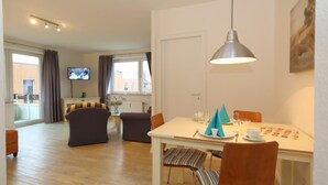 A modern living room with a dining area, a flat-screen TV, and a large window. - Appartement Kiek in 09 Westerland (Westerland)