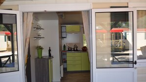 A compact kitchen with green cabinets, a wooden countertop, and a small dining area with a table and chairs. - Victoria Mobilehome Camping Dole (Podgora)