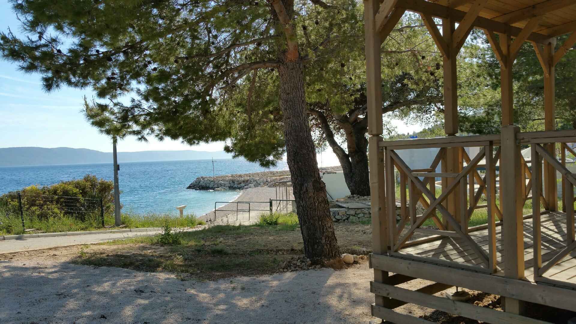 A wooden gazebo overlooking a beach with a clear view of the sea and distant hills.