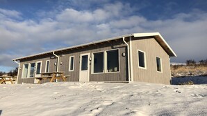 A wooden cabin with large windows and a picnic table in a snowy landscape. - Hvammstangi Hill Homes (Hvammstangi)