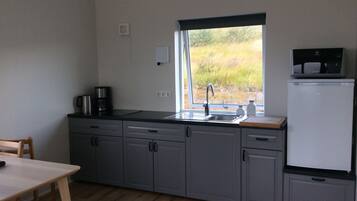 A compact kitchen with grey cabinets, a sink, a coffee maker, a microwave, and a refrigerator.