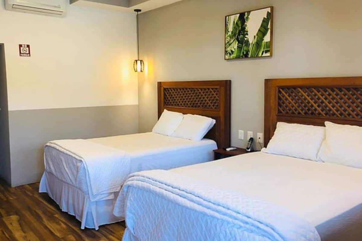 A hotel room with two single beds, a wooden headboard, a wall-mounted light, and a small painting.