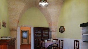 Un coin repas avec une table dressée pour quatre personnes, entouré de chaises en bois, d’un sol carrelé et d’une arche en pierre.
