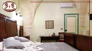 Un lit bien fait, avec des oreillers et des serviettes pliées, une table de chevet en bois, un bureau avec une lampe et une porte dotée d’un cadre vert.