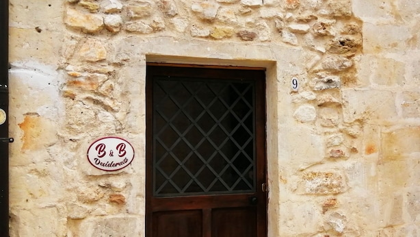 Un bâtiment en pierre avec une porte en bois et une petite fenêtre. Une enseigne portant l’inscription « B&B Desiderato » est visible sur le mur.