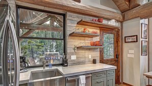 A modern kitchen with a large window, stainless steel appliances, and wooden accents. - SkyRun Cabin - Stunning Mountain Views & Fire Pit (Golden)