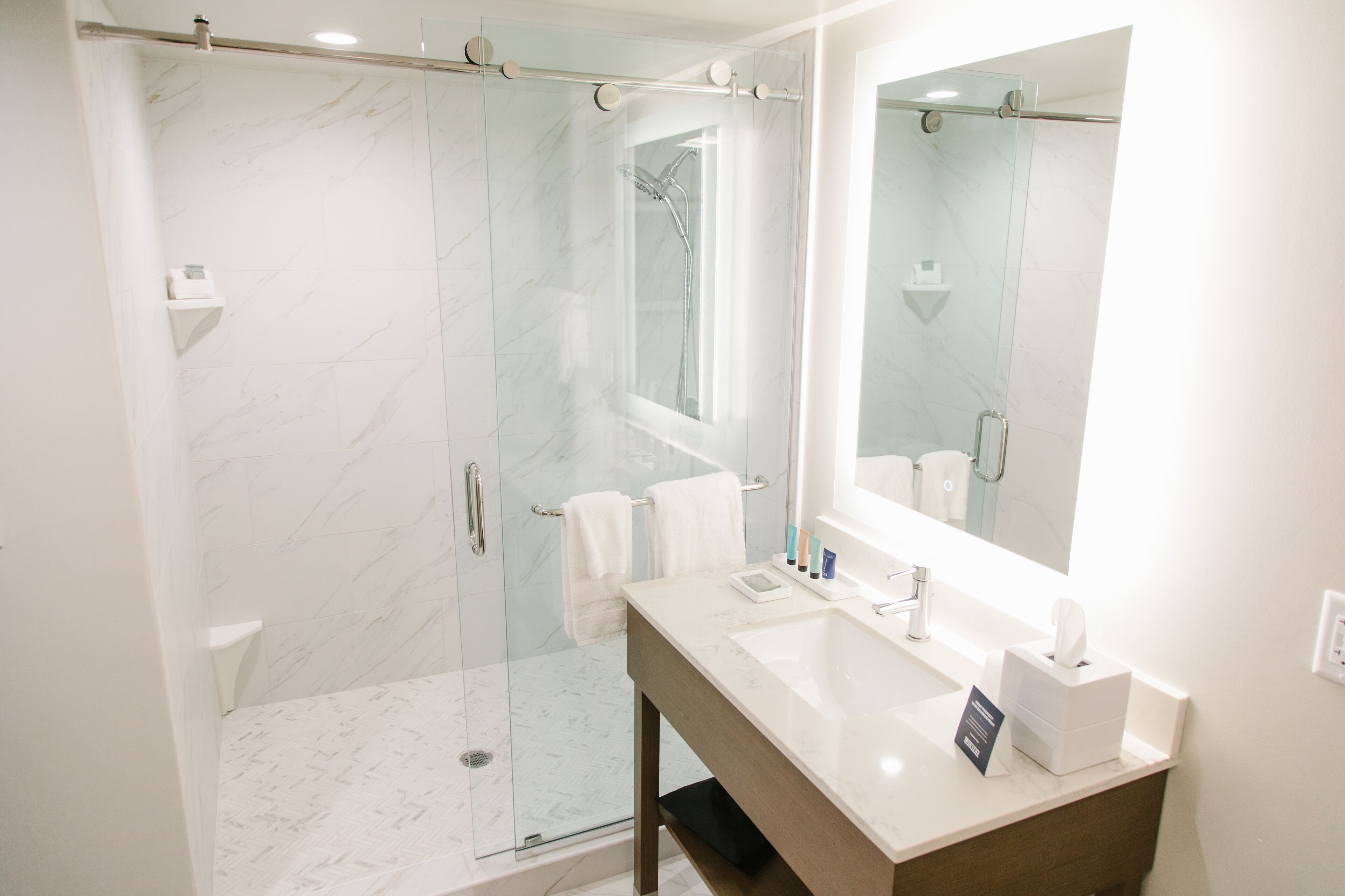 Une salle de bain moderne avec une douche à parois de verre, un grand miroir et un meuble-lavabo recouvert de carreaux de marbre.