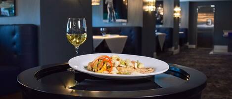 Une table à manger avec une assiette de nourriture et un verre de vin blanc, dans l’intimité d’un restaurant à la lumière tamisée.