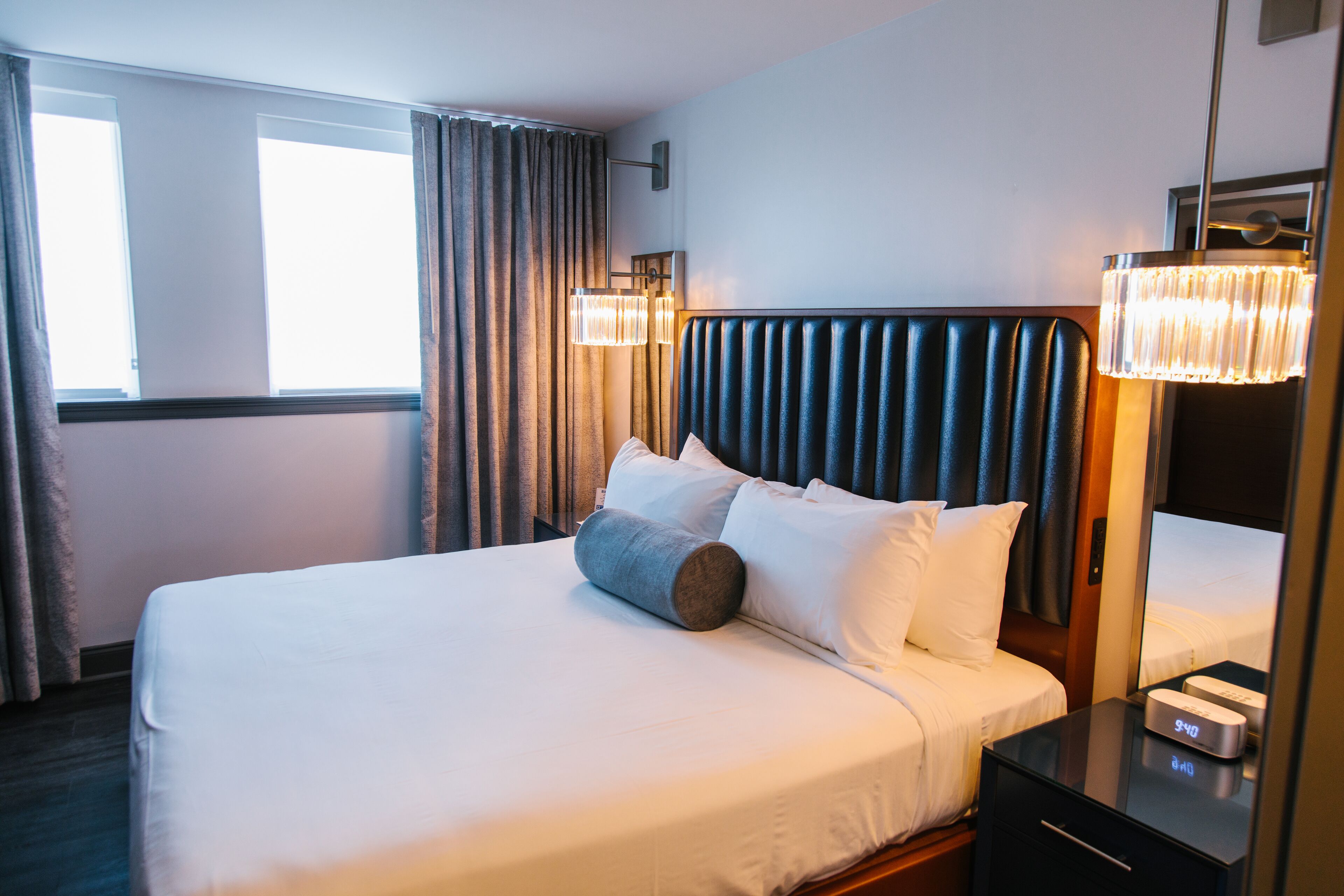 A hotel room with a large bed, a bedside table with a clock, and a window with curtains.