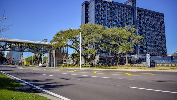 A modern hotel with a prominent glass facade, a parking lot, and a clear blue sky. - The Hotel Legends (Biloxi)