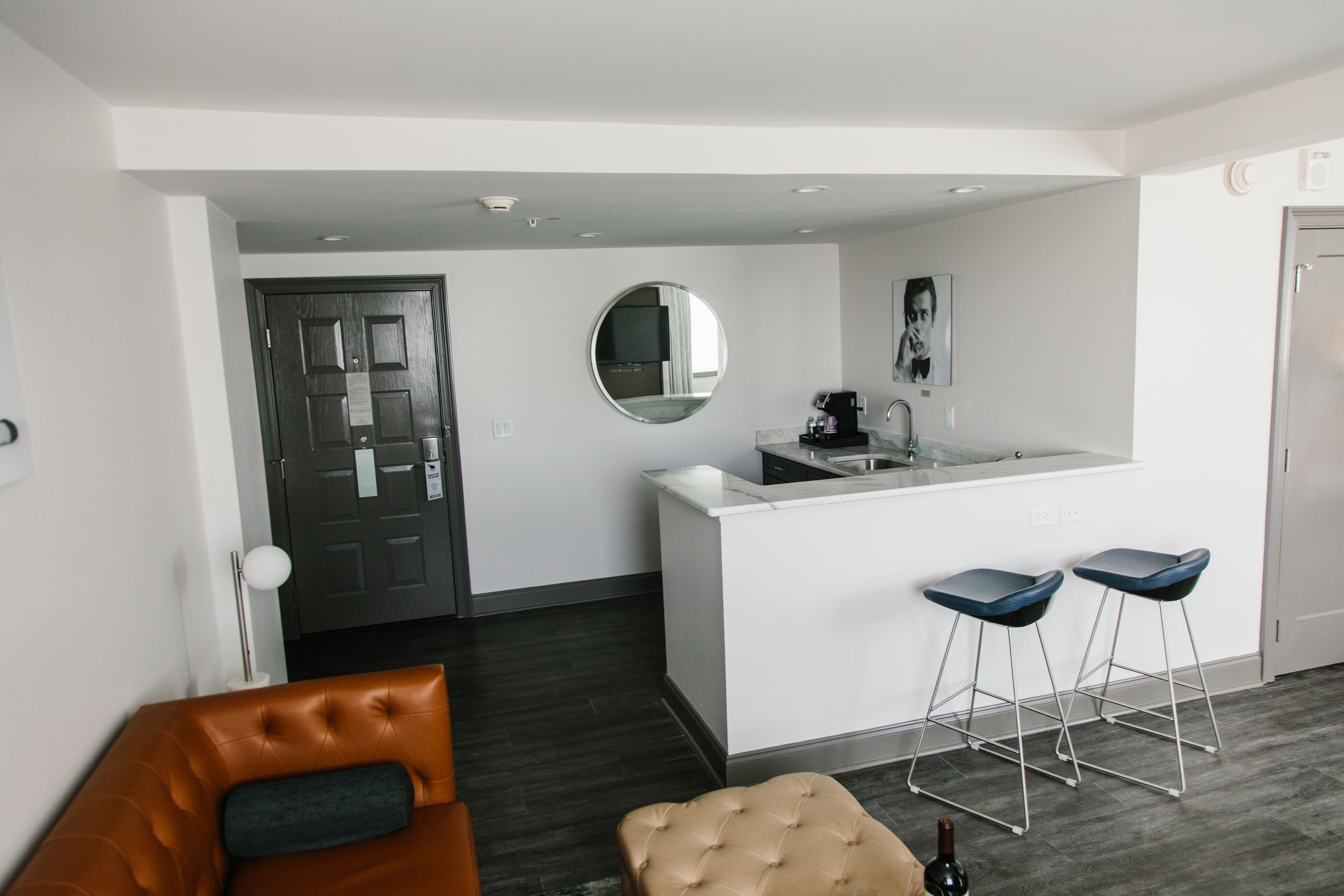 A modern kitchen with a round mirror, a coffee machine, and two bar stools.