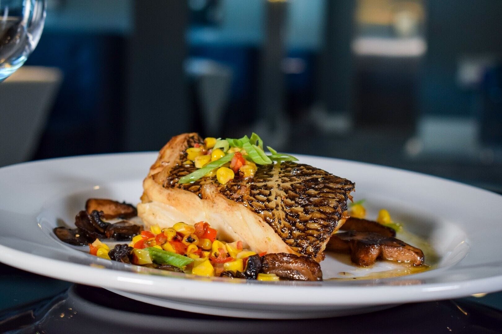Une assiette contenant un poisson grillé, des champignons et un assortiment de légumes colorés en guise de garniture.