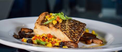 A plate with a grilled fish, mushrooms, and a colorful vegetable garnish.