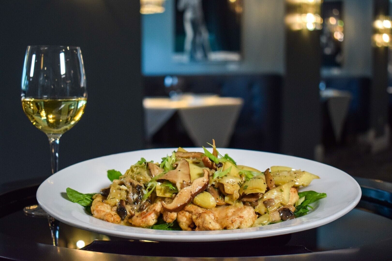 A plate of food with a glass of white wine on a table in a restaurant.