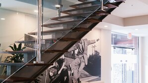 A modern interior with a glass staircase, a beige sofa, and a large wall mural. - The Hotel Legends (Biloxi)