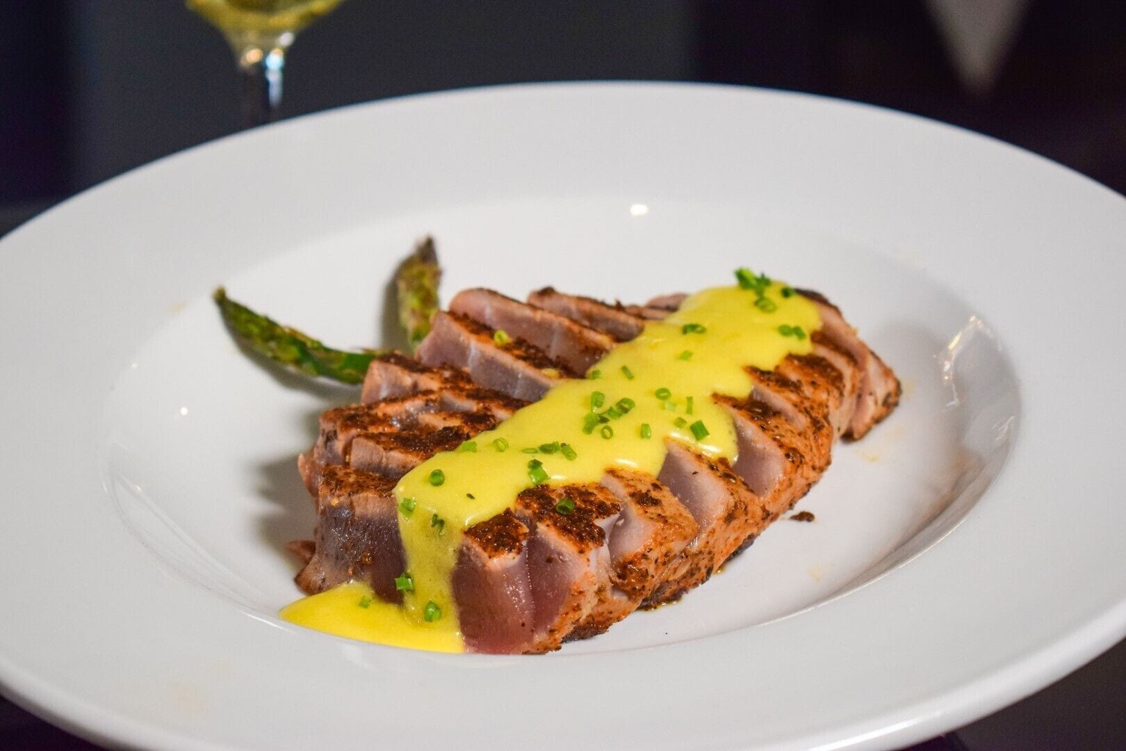 A plate with sliced meat topped with yellow sauce and green garnish.