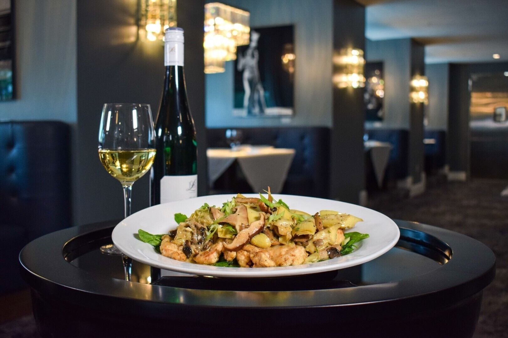 A dining table with a plate of food and two glasses of wine in a restaurant setting.