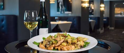 A dining table with a plate of food and two glasses of wine in a restaurant setting.