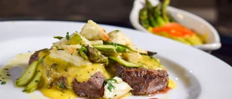 A plate of food with a steak and vegetables, possibly asparagus, on a white plate.