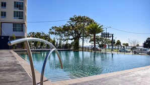 A swimming pool with a wooden deck and metal railings, surrounded by trees and a building in the background. - The Hotel Legends (Biloxi)