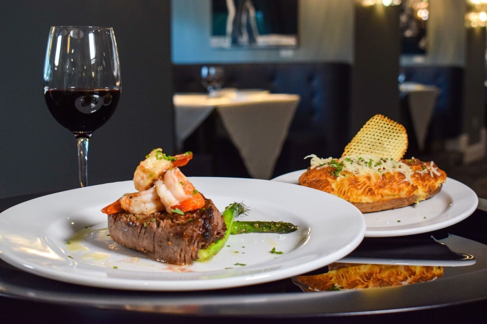 A dining table with two plates of food, a glass of red wine, and a candle.