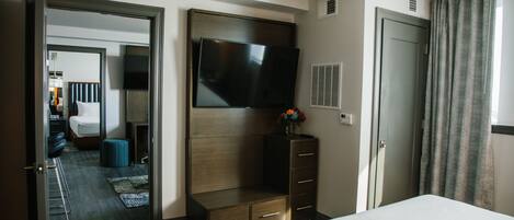 A hotel room with a bed, a TV mounted on the wall, a dresser, and a door leading to another room.