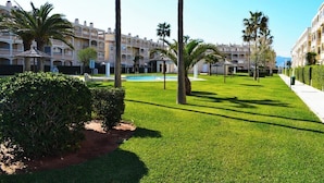 A well-maintained courtyard with a swimming pool, palm trees, and a building with balconies. - Anacasa Bahia de Denia Les Marines AP2102 (Denia)