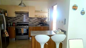 A modern kitchen with a central island, stainless steel appliances, and wooden cabinets. - Summer paradise, total relaxation on your vacation (Stgo)