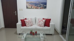 A white sofa with red and white patterned cushions, a glass coffee table with decorative items, and a cityscape painting on the wall. - Summer paradise, total relaxation on your vacation (Stgo)