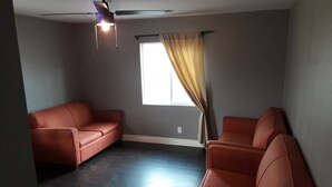 Une pièce avec un plancher en bois foncé, un ventilateur de plafond et deux canapés rouges.