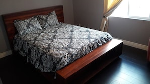 Un lit recouvert d’une couvre-lit à motifs, dans une pièce dotée d’un plancher en bois et d’une fenêtre ornée de rideaux.