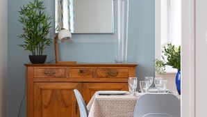 A dining area with a wooden cabinet, a table set with plates and glasses, a chair, and a potted plant. - Le Hauban - Three Bedroom Apartment, Sleeps 6 (Saint-Malo)