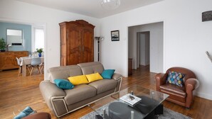 A living room with a beige sofa, a glass coffee table, a brown leather armchair, and a wooden cabinet. - Le Hauban - Three Bedroom Apartment, Sleeps 6 (Saint-Malo)