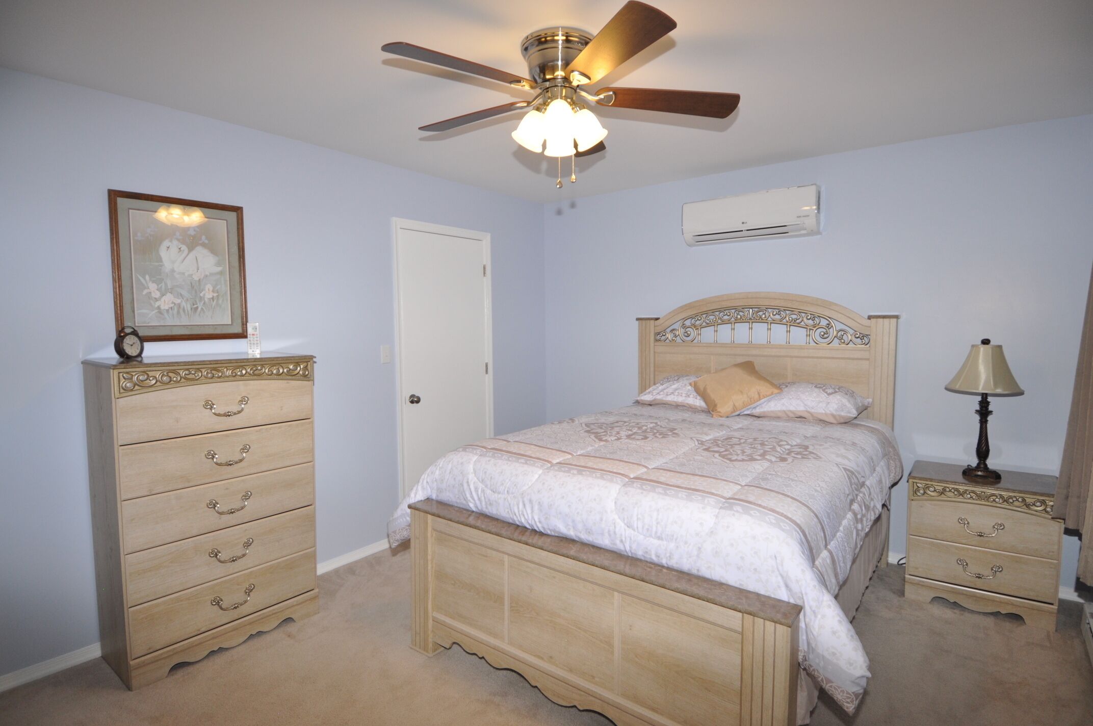 Een slaapkamer met een bed, een dressoir, nachtkastje, plafondventilator en een airconditioning.