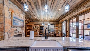 A rustic kitchen with a stone wall, wooden ceiling, and a large window.