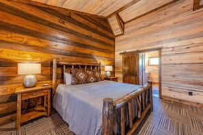 Un dormitorio tipo cabaña de troncos con una cama de madera, dos mesitas de noche con lámparas y un ventanal grande.