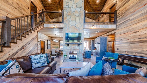 A spacious living area with a stone fireplace, leather sofas, and a dining area with a high ceiling and wooden beams.
