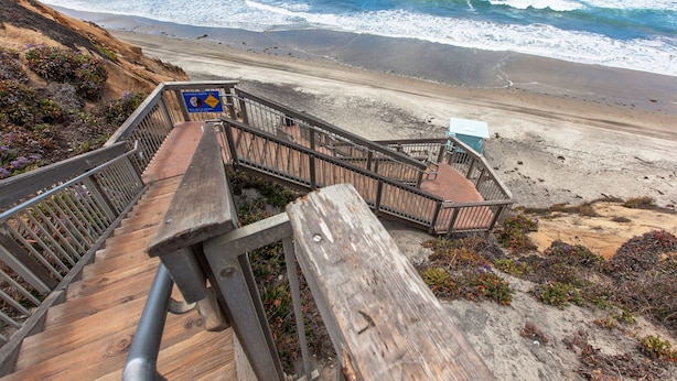 Una escalera de madera que lleva a una playa, con un letrero que indica vistas al acantilado.
