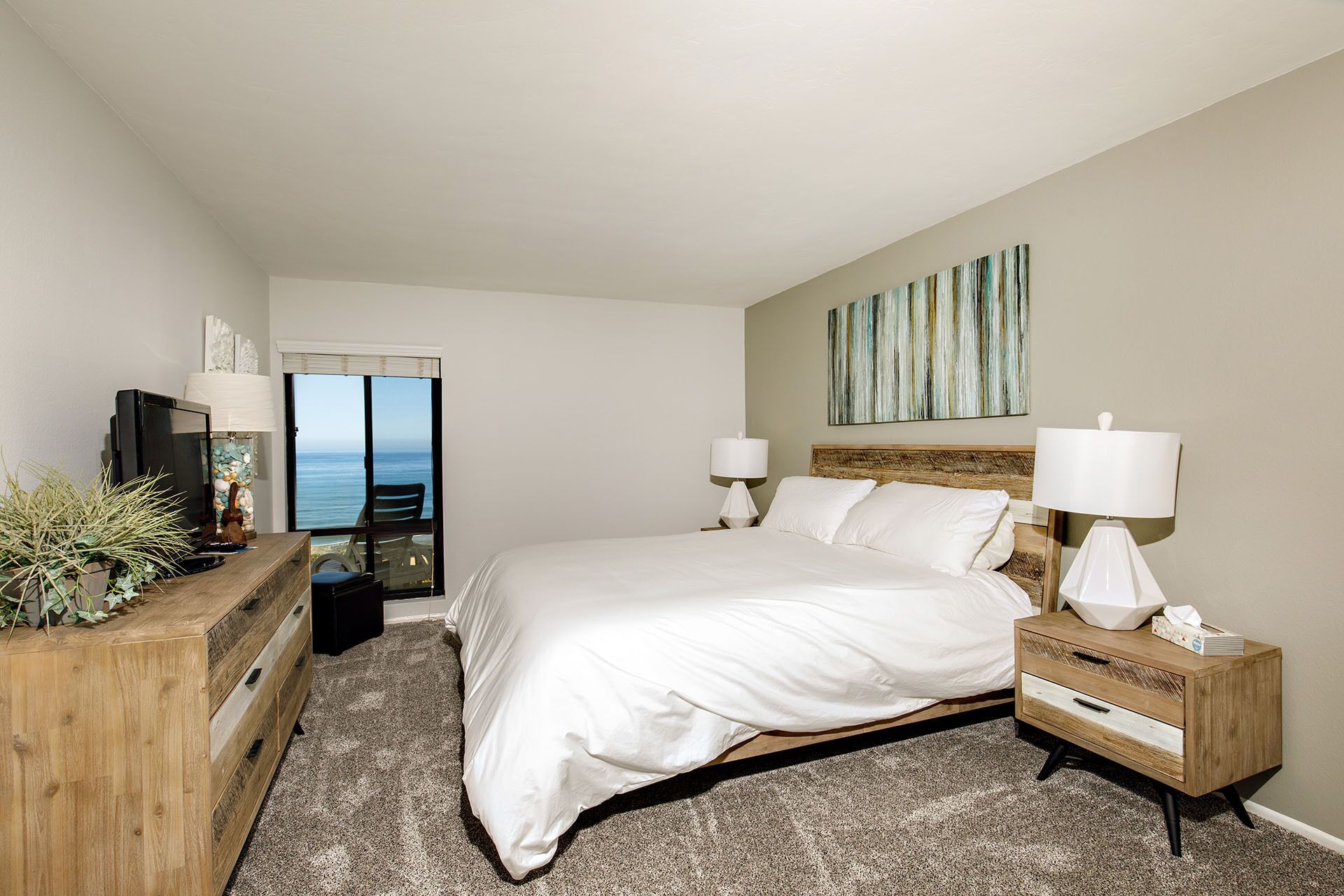 A bedroom with a large bed, two bedside lamps, a wooden nightstand, a dresser, and a television.