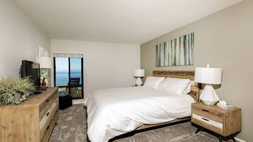 A bedroom with a large bed, two bedside lamps, a wooden nightstand, a dresser, and a television.