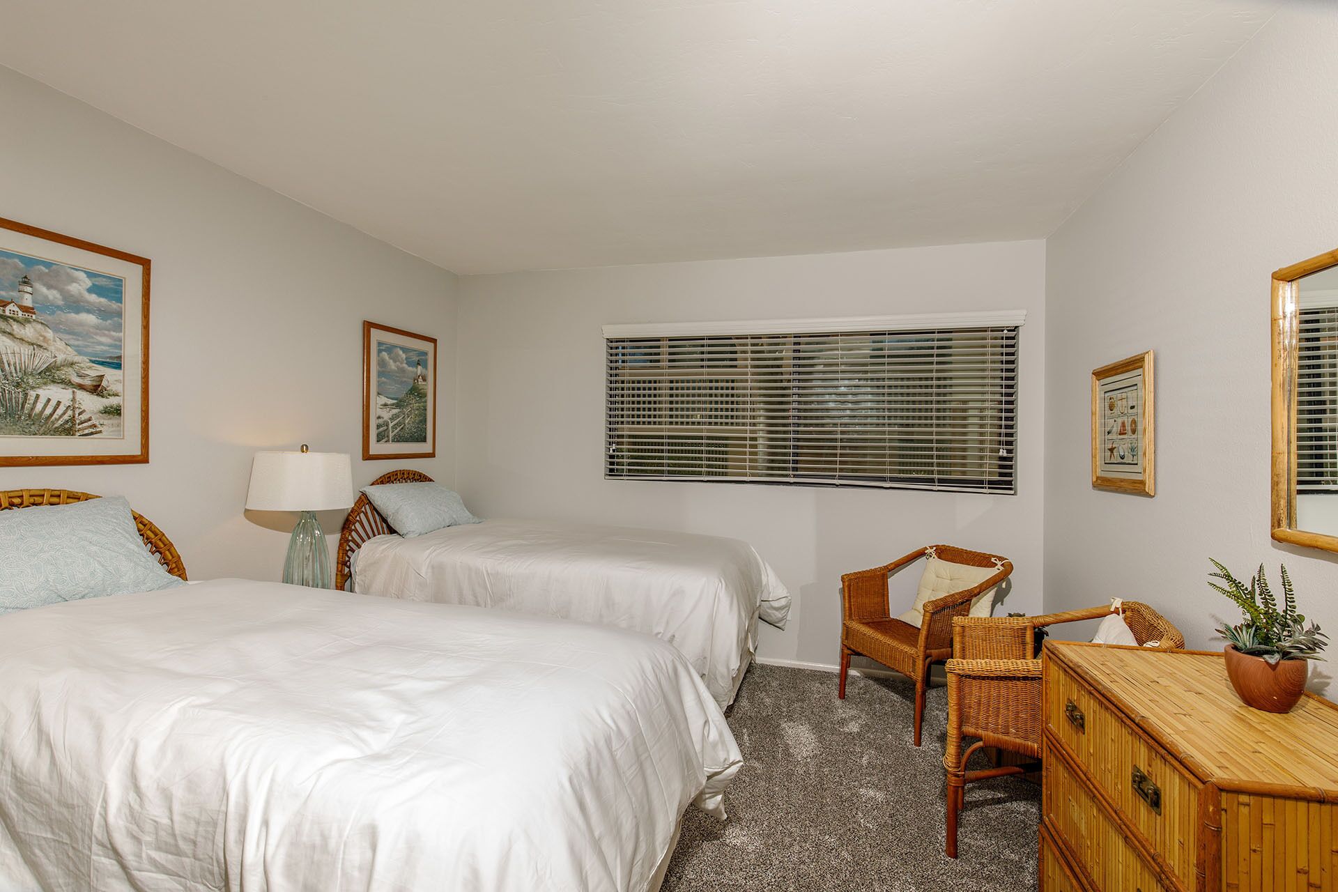 A bedroom with two beds, a window with blinds, a chair, a dresser, and framed pictures on the walls.