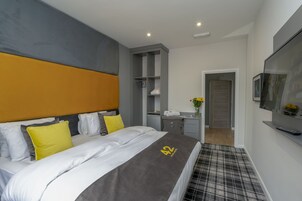 Quarto de hotel moderno com cama grande, escrivaninha, guarda-roupa e televisão.