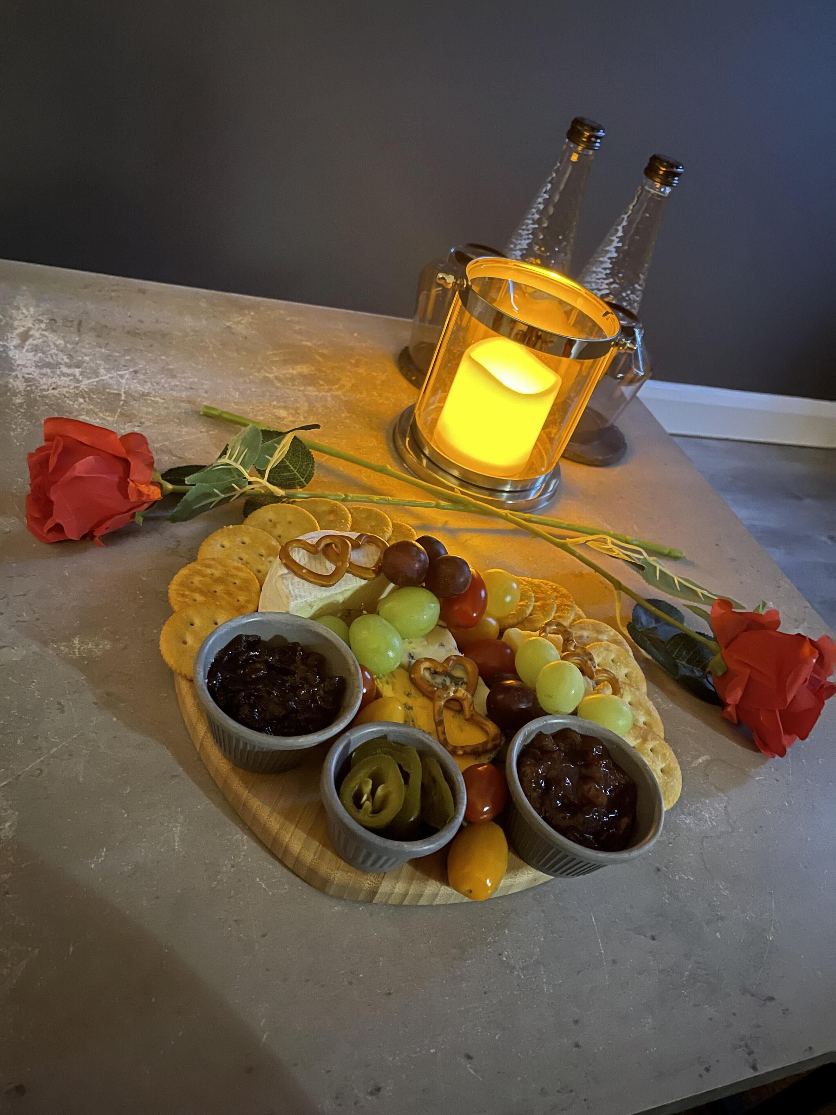 Un tavolo con un tagliere di formaggi, cracker, grappoli d'uva e una candela accesa.