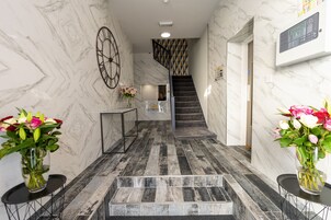 Um corredor com piso de mármore, com uma mesa de recepção, um relógio e uma escada com paredes de padrão geométrico.