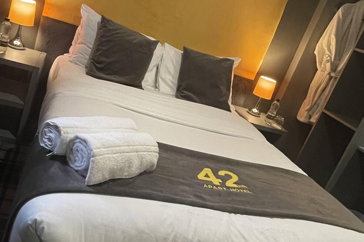 A hotel room with a large bed, a headboard, two bedside tables with lamps, and a robe hanging on the wall.