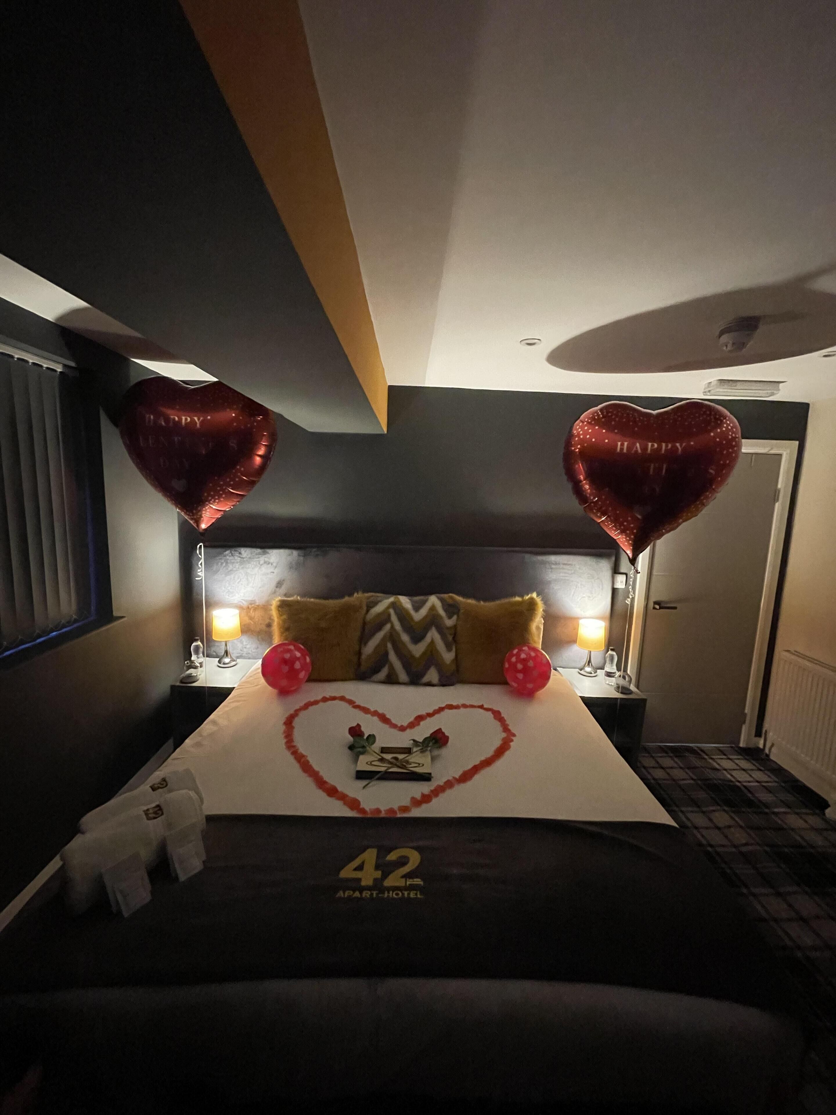 A hotel room with a bed, heart-shaped decorations, and a number '42' on the bedspread.