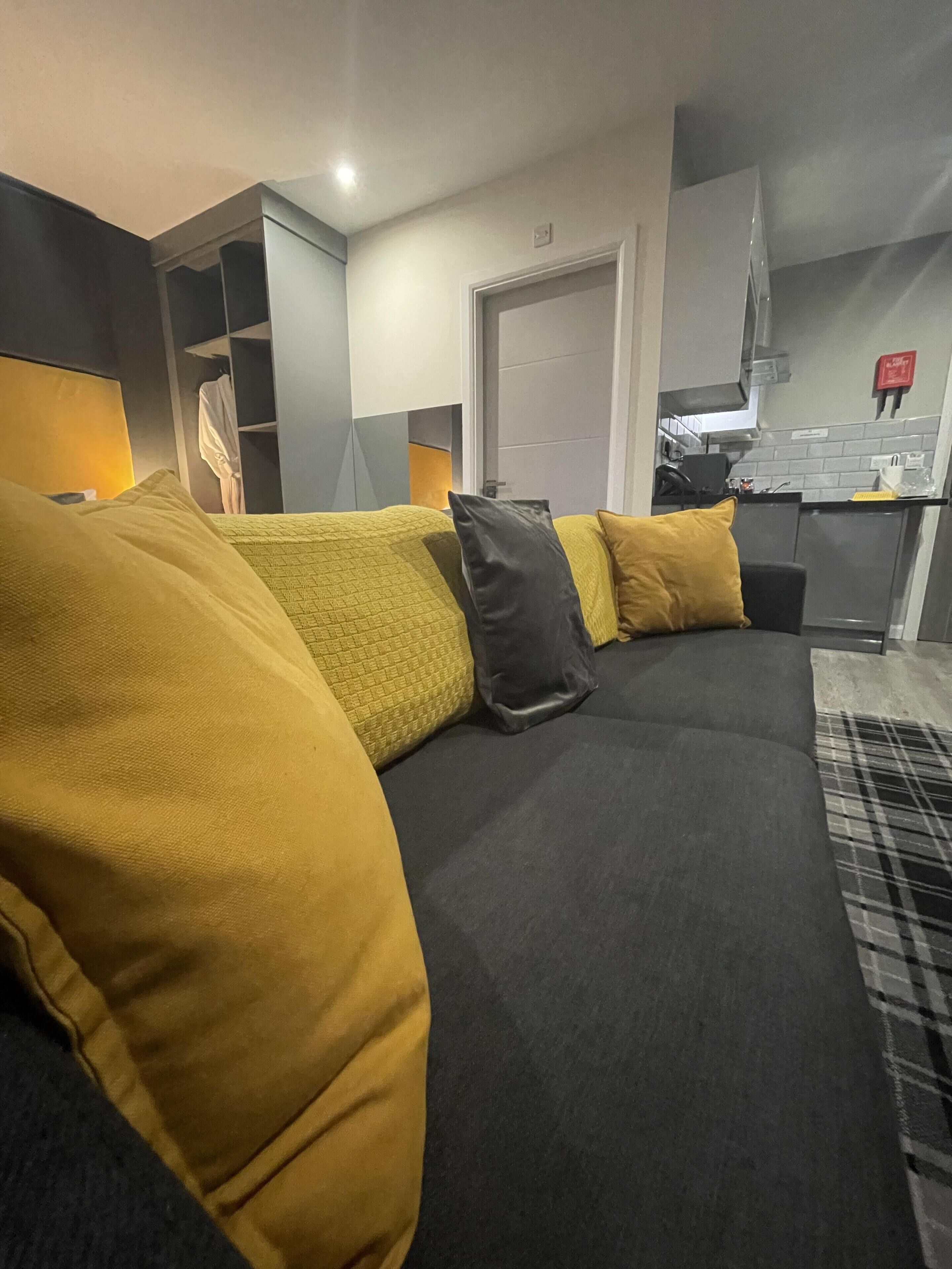 A modern living room with a dark grey sofa, yellow cushions, and a plaid rug.